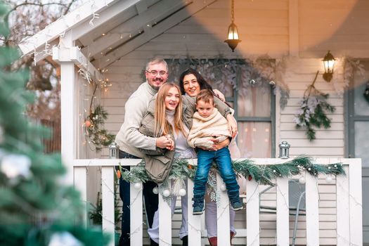 Happy family on the porch of the Christmas decorated house, snowing outdoor. Happy New Year and Merry Christmas. Magic winter