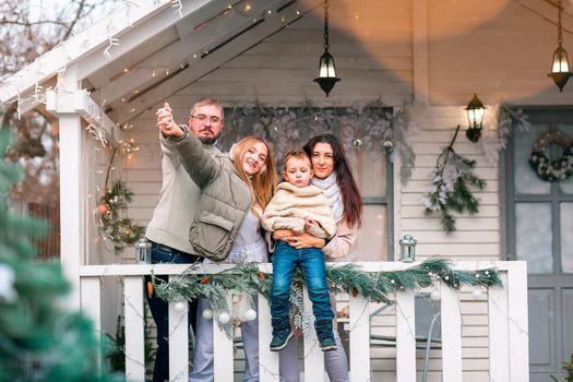 Happy family on the porch of the Christmas decorated house, snowing outdoor. Happy New Year and Merry Christmas. Magic winter