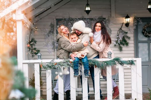 Happy family on the porch of the Christmas decorated house, snowing outdoor. Happy New Year and Merry Christmas. Magic winter