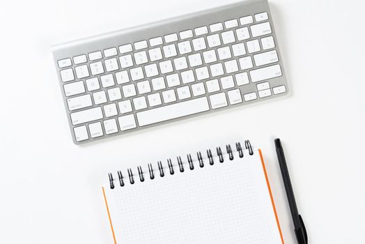 Top view of businessman workplace. Spiral notepad, pen and computer keyboard on white surface. Education, creativity and working concept with copy space. Finance and investment background.