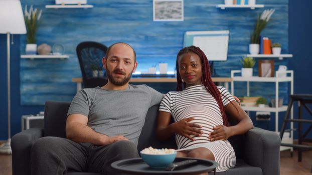 Pregnant interracial couple using video call conference for remote online communication at home. Mixed race people expecting baby, talking to friends with technology in living room