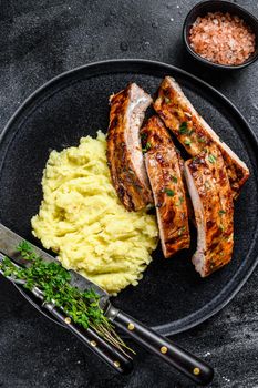 Sliced BBQ grilled pork rack spare ribs on a plate with mash potato. Black background. Top view.