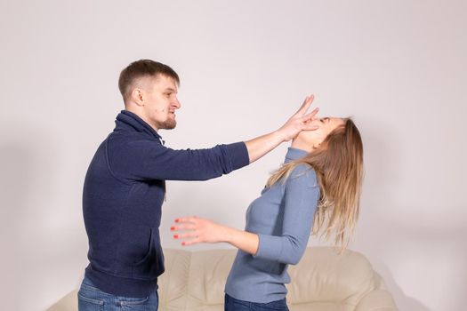 people, domestic violence and abuse concept - young man threatens his wife with his fist on white background.