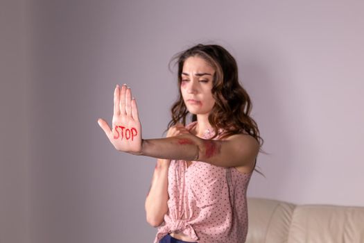 Domestic violence, protesting and people concept - brunette woman expressing denial with STOP on her hand on grey room.