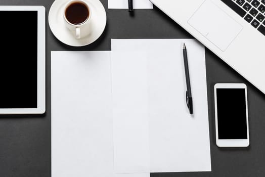 Top view of designer workplace with modern digital devices. Flat lay stylish design with black surface and copy space. Digital technology and mobile lifestyle. Laptop, tablet computer and smartphone.