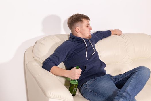 Depression and alcoholism concept - aggressive young man sitting on a sofa with bottle of alcohol.