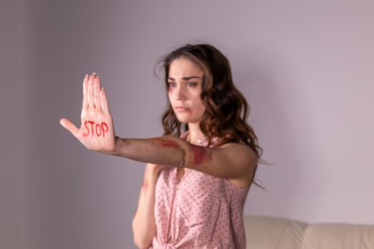 Domestic violence, protesting and people concept - brunette woman expressing denial with STOP on her hand on grey room.