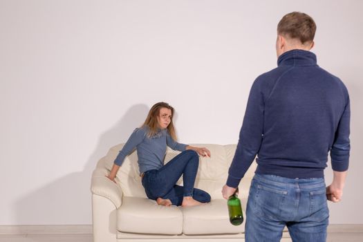 People, violence, alcoholism and abuse concept - Man with bottle alcohol while wife is lying on sofa.