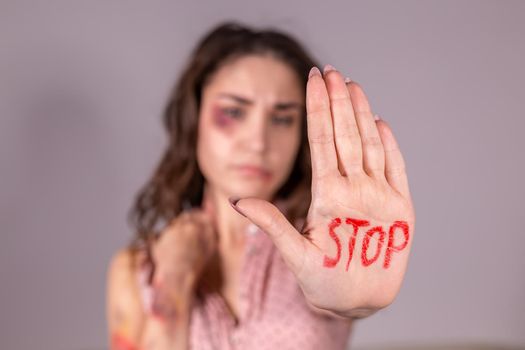 Domestic violence, protesting and people concept - brunette woman expressing denial with STOP on her hand on grey room.