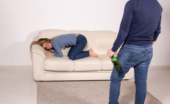 People, violence and abuse concept - Man drinking alcohol while wife is lying on sofa.