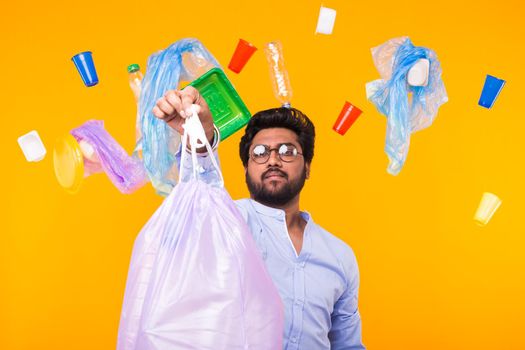 Environmental pollution, plastic recycling problem and ecology problem concept - sad indian man holding garbage bag on yellow background