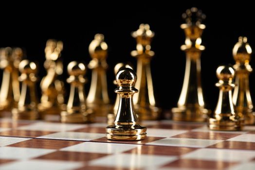 Golden chess figures standing on wooden chessboard. Intellectual duel and tactical battle in business. Strategy planning and leadership concept. Gold metal chess pieces in row on black background.