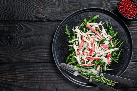 Crab meat on a plate with arugula. Black background. Top view. Copy space.