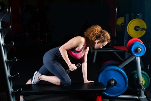 Woman bodybuilder engaged with dumbbells in the gym.