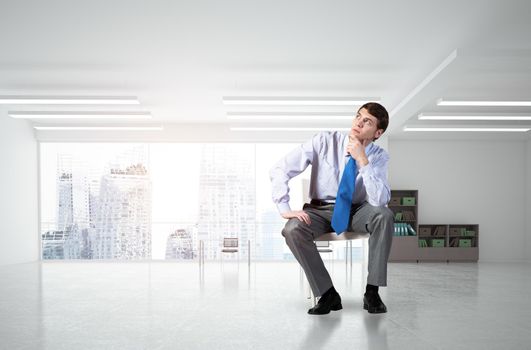 young businessman sits on an office chair, thoughtful and looking up