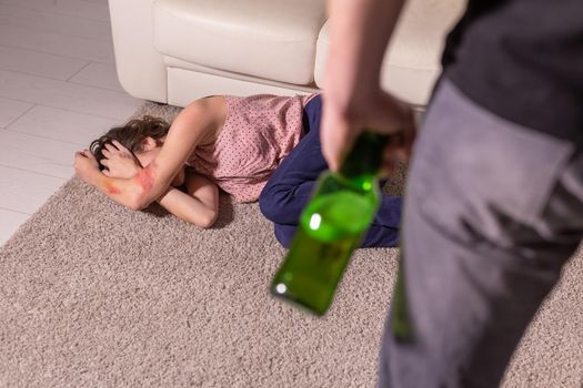 Alcoholism, abuse and domestic violence - Woman lying on the floor. She is afraid of man with bottle.