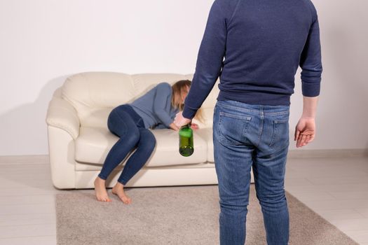 People, violence and abuse concept - Man drinking alcohol while wife is lying on sofa.