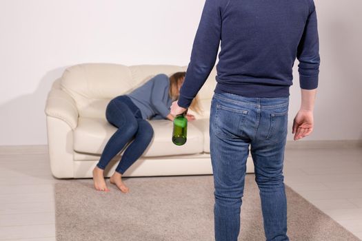 People, violence and abuse concept - Man drinking alcohol while wife is lying on sofa.