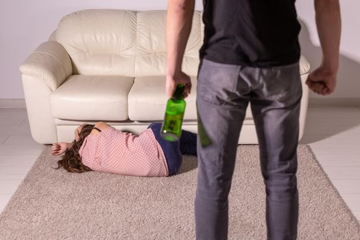 domestic violence, alcoholic and abuse concept - drunk man with bottle abusing his wife lying on the floor.