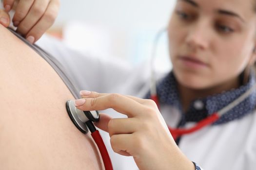 Close-up of young female doctor listen to patients back with stethoscope tool. Concentrated intern examine body, diagnostic in clinic. Medicine concept