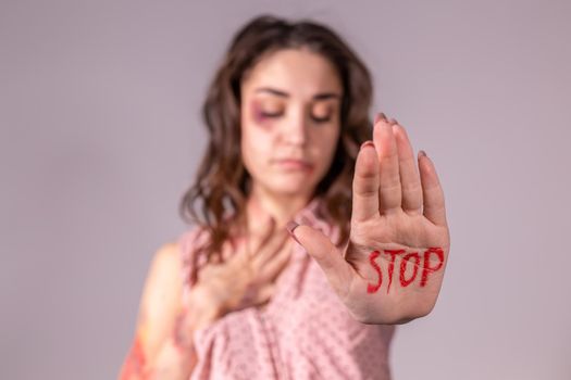 Domestic violence, protesting and people concept - brunette woman expressing denial with STOP on her hand on grey room.