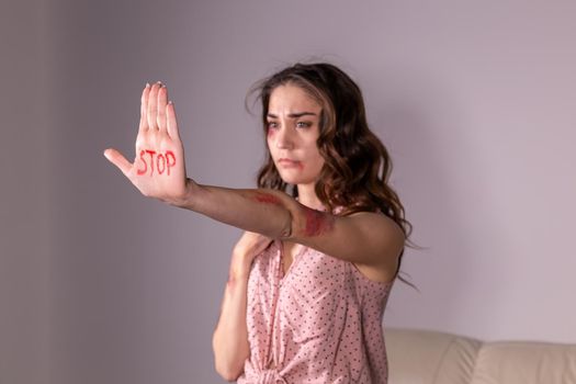 Domestic violence, protesting and people concept - brunette woman expressing denial with STOP on her hand on grey room.