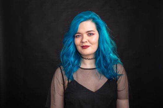 people, fashion and hair concept - close-up portrait of young woman in black dress with blue hair on black .