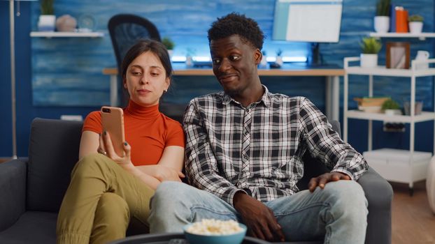 Young interracial couple talking on video call with camera at home. Mixed race people using online conference for remote communication in living room. Married partners with technology