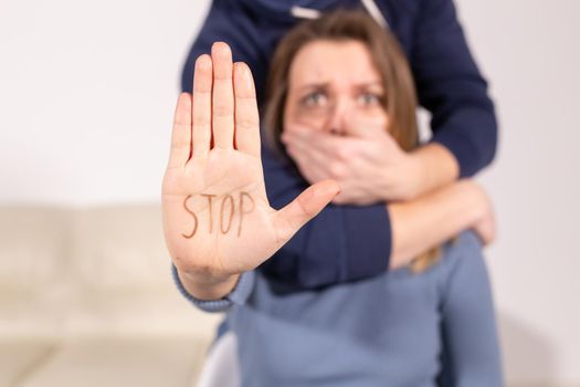 People, domestic violence and abuse concept - Woman shows stop abusing sign. Man covers her mouth with her hand.