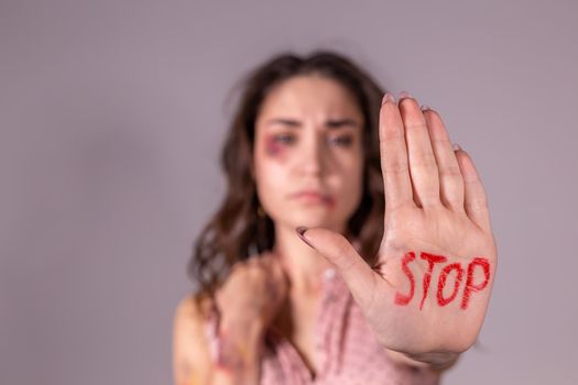 Domestic violence, protesting and people concept - brunette woman expressing denial with STOP on her hand on grey room.