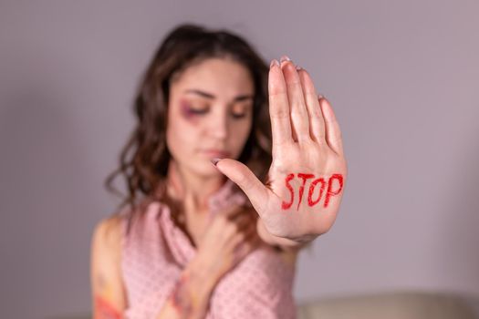 Domestic violence, protesting and people concept - brunette woman expressing denial with STOP on her hand on grey room.