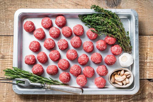 Uncooked Raw beef and pork meatballs with thyme and rosemary in kitchen tray. Wooden background. Top view.