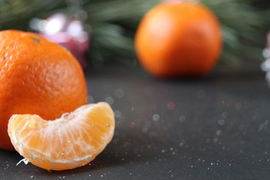 mandarin whole in the peel and a slice of fruit lie side by side on a black background next to a branch of spruce and a silver cone. New Year and Christmas. holiday attribute.