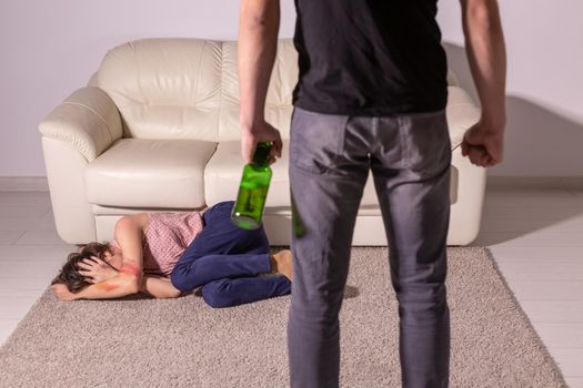 Alcoholism, abuse and domestic violence - Woman lying on the floor, afraid of men with bottle.