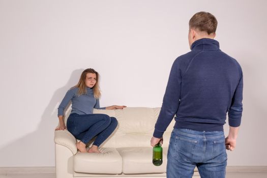 People, violence, alcoholism and abuse concept - Man with bottle alcohol while wife is lying on sofa.