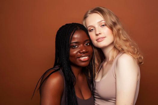 two pretty girls african and caucasian blond posing cheerful together on brown background, ethnicity diverse lifestyle people concept close up