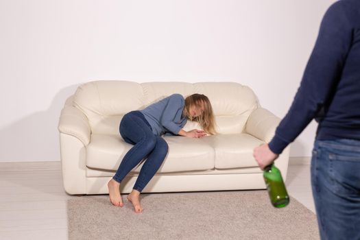 People, violence and abuse concept - Man drinking alcohol while wife is lying on sofa.