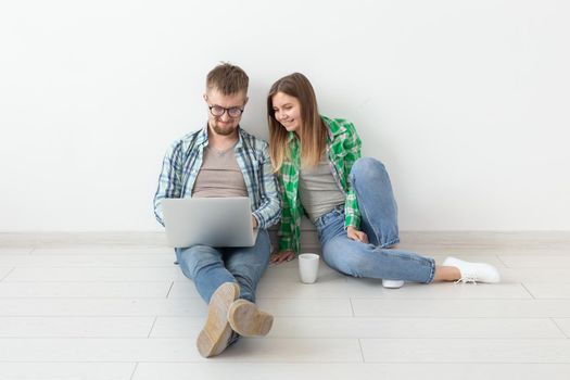Smiling young couple makes online purchases of furniture in their new mortgage apartment. Online shopping concept with laptop and gadgets. Copyspace