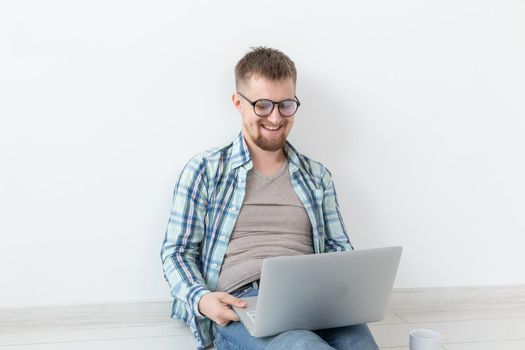Positive young man in casual clothes surfing the Internet in search of new housing sitting on the floor in an empty room. The concept of finding an apartment using the Internet and a laptop. Copyspace