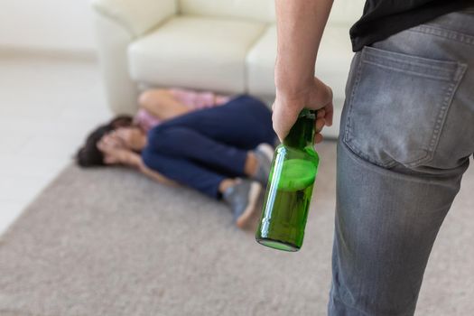 Victim, domestic violence, abuse and alcoholic concept - drunk man with bottle near his wife lying on the floor.