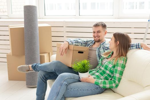 Positive crazy cheerful couple rejoices in moving their new apartment sitting in the living room with their belongings. Concept of housewarming and mortgages for a young family