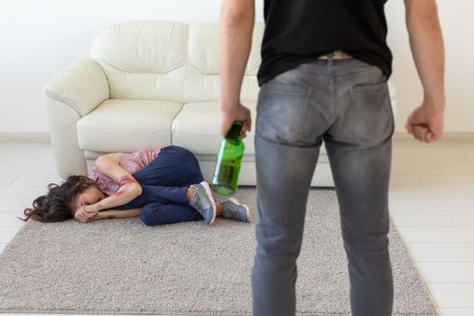 domestic violence, alcoholic and abuse concept - drunk man with bottle abusing his wife lying on the floor.