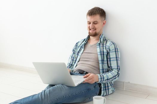 Positive young man in casual clothes and glasses surfing the Internet using Wi-Fi and a laptop in search of rental housing. Housewarming and apartment search concept