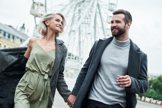 Romantic date outdoors. Young couple running at entertainment park holding hands looking at each other smiling happy close-up