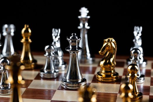 Gold and silver chess figures placed on wooden chessboard. Intellectual duel and tactical battle in business. Strategy planning, leadership and teamwork concept. Close-up metal chess pieces on board.