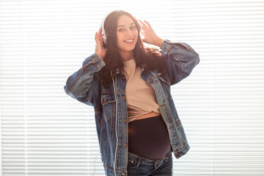 Young peaceful pregnant woman listens to pleasant classical music using smartphone and headphones. Concept of positive attitude before childbirth