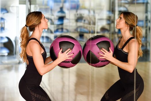 Woman lifting fitballs in the gym. Young girl wearing sportswear clothes in front of a mirror.