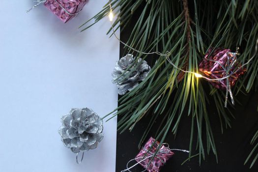 a white sheet of paper next to a branch of its pine tree next to a garland cone with space for text and with copyspace.