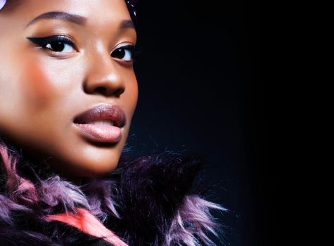 young pretty african american woman in spotted fur coat and flowers on head smiling on black background, fashion people concept close up