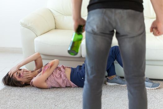 Victim, domestic violence, abuse and alcoholic concept - drunk man with bottle near his wife lying on the floor.